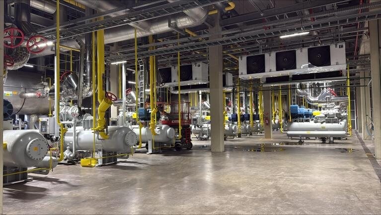Interior da casa de máquinas, com tubulação de amônia e compressores industriais alinhados